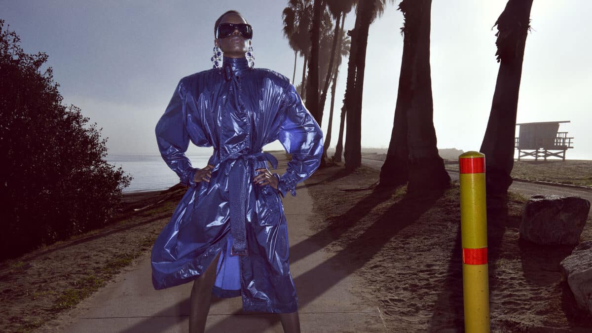 A model in a glossy blue coat and oversized black sunglasses