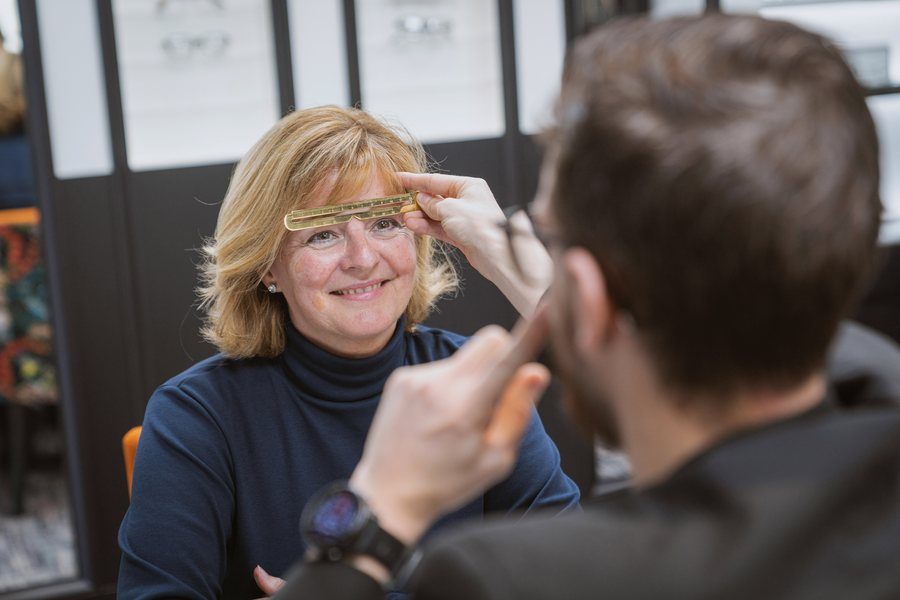 A dispensing optician fitting new frames for a smiling patient