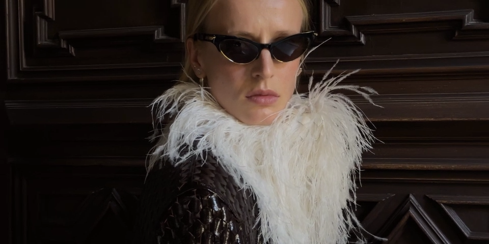 Model in black cat-eye Bottega Veneta sunglasses and a white feather stole (still from the Summer 2026 film)