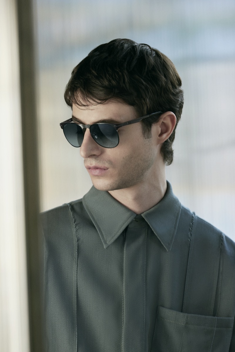 Man in Persol 649 sunglasses and a grey-green shirt beside a window