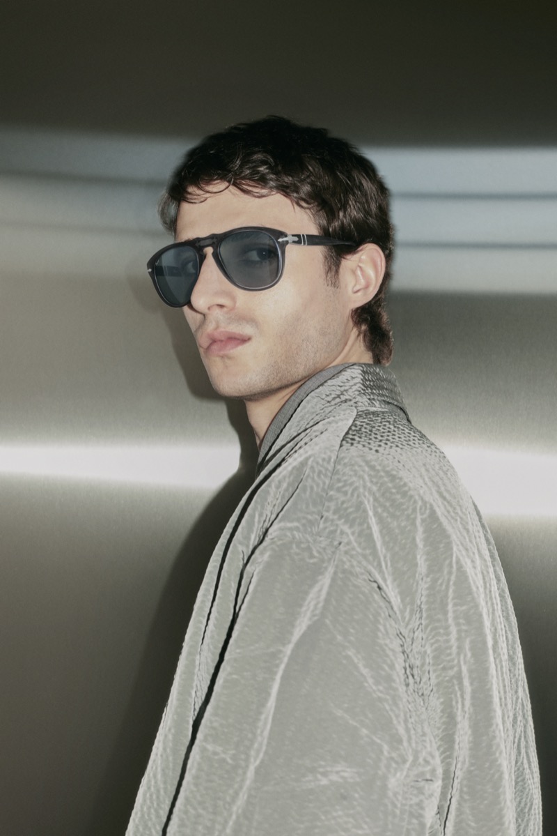Man in Persol 649 sunglasses and a silver jacket against a metal wall