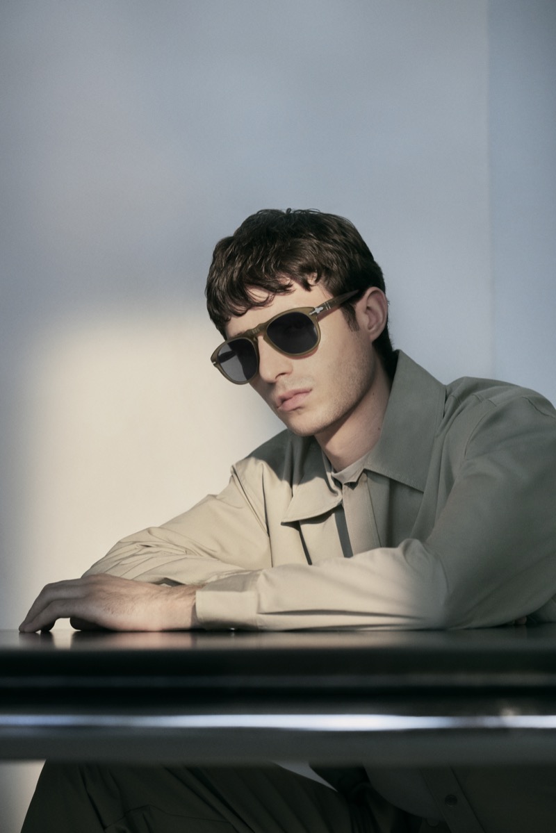 Man in Persol 649 sunglasses seated at a desk in a beige shirt